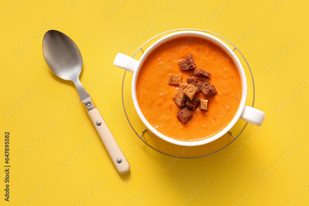 Pot of tasty cream soup with croutons on yellow background