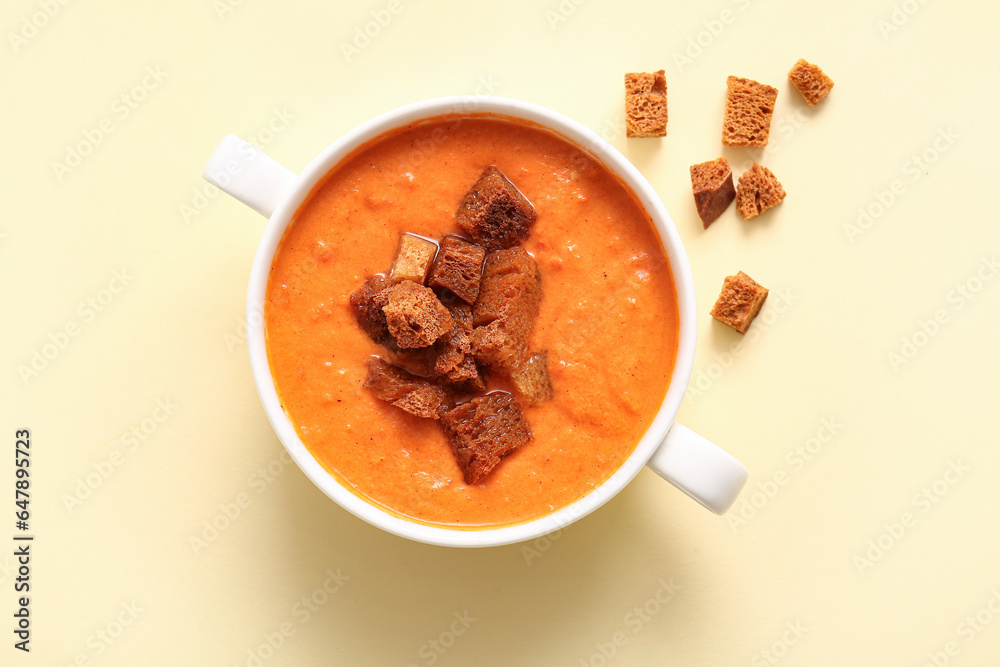 Pot of tasty cream soup with croutons on yellow background