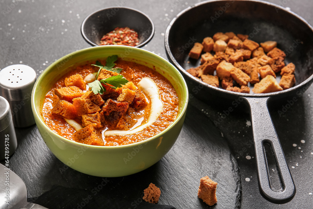 Bowl of tasty cream soup with croutons on black background