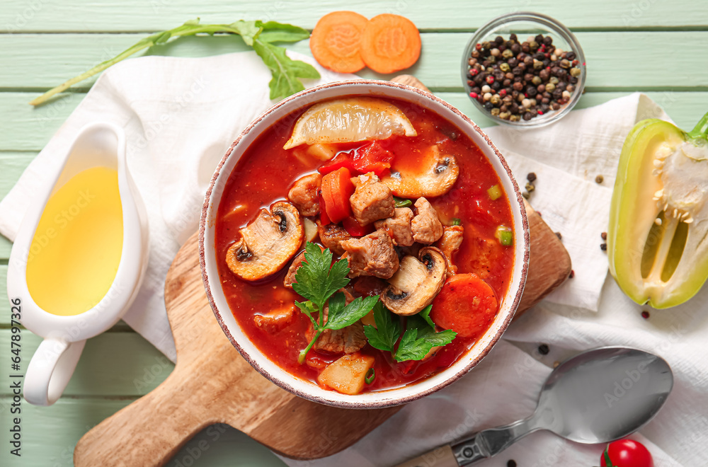 Bowl of tasty beef stew and ingredients on green wooden background