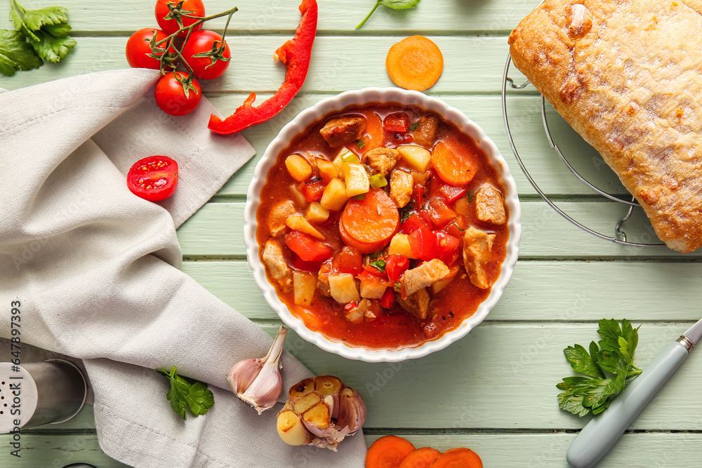 Bowl of tasty beef stew and ingredients on green wooden background