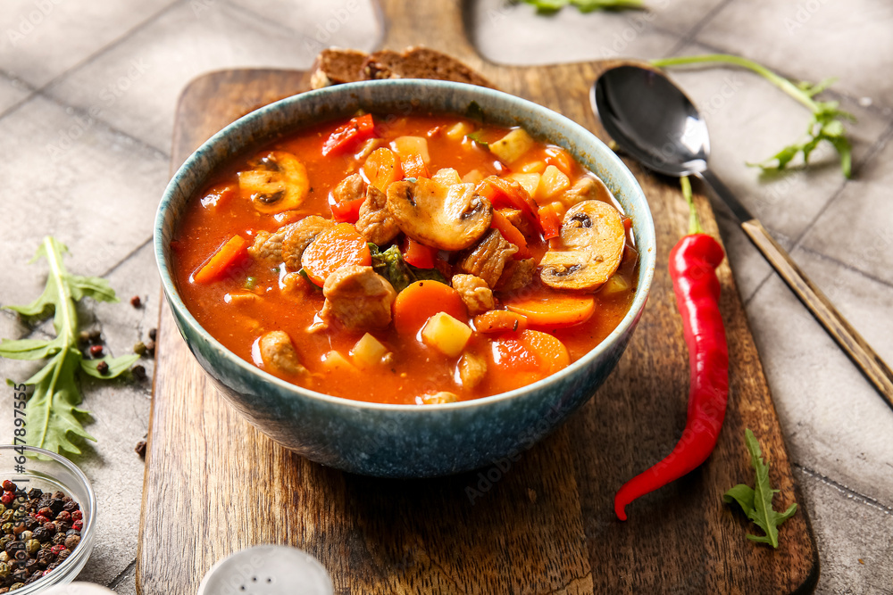 Bowl of tasty beef stew on grey tile background