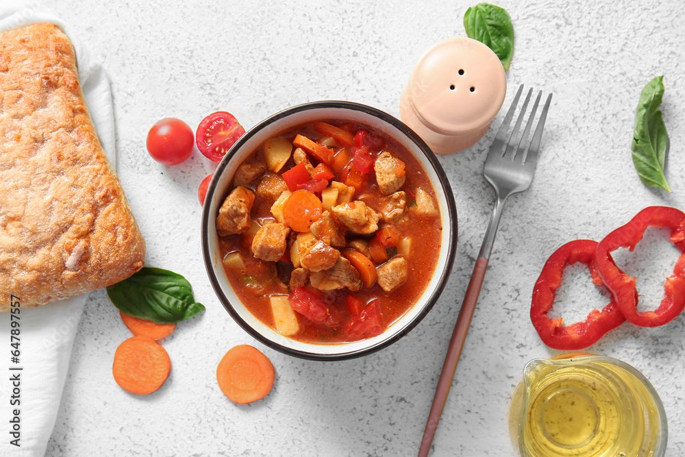 Bowl of tasty beef stew and fresh vegetables on light background