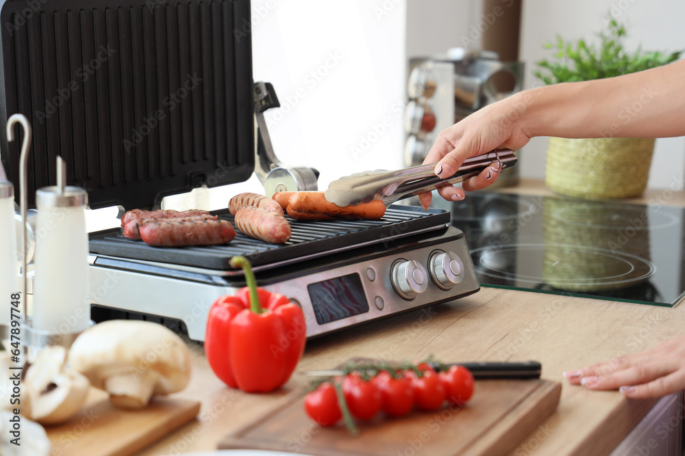 Woman cooking delicious sausages on modern electric grill in kitchen, closeup