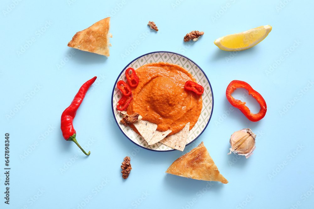 Plate of tasty muhammara and ingredients on blue background