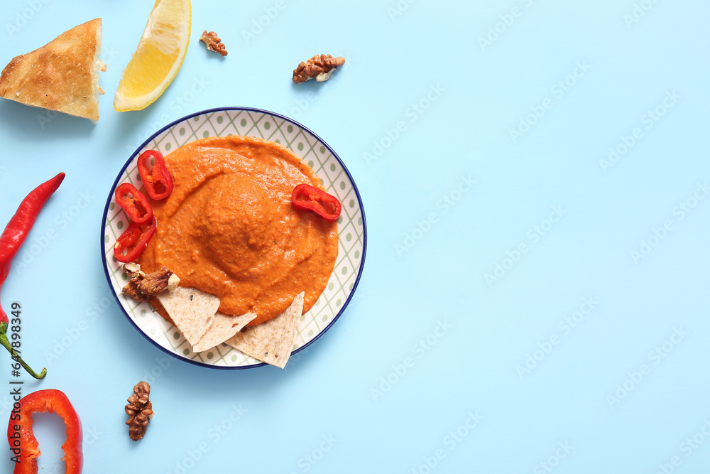 Plate of tasty muhammara and ingredients on blue background