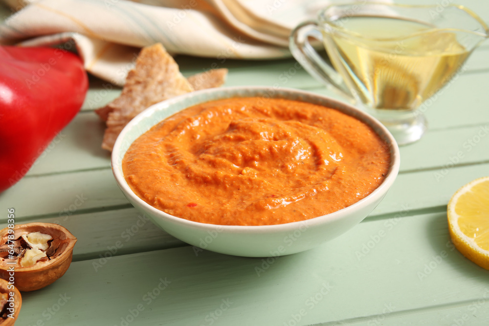 Bowl of tasty muhammara on green wooden background