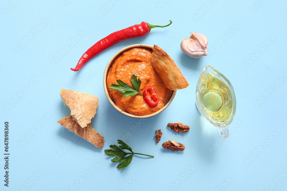 Bowl of tasty muhammara and ingredients on blue background