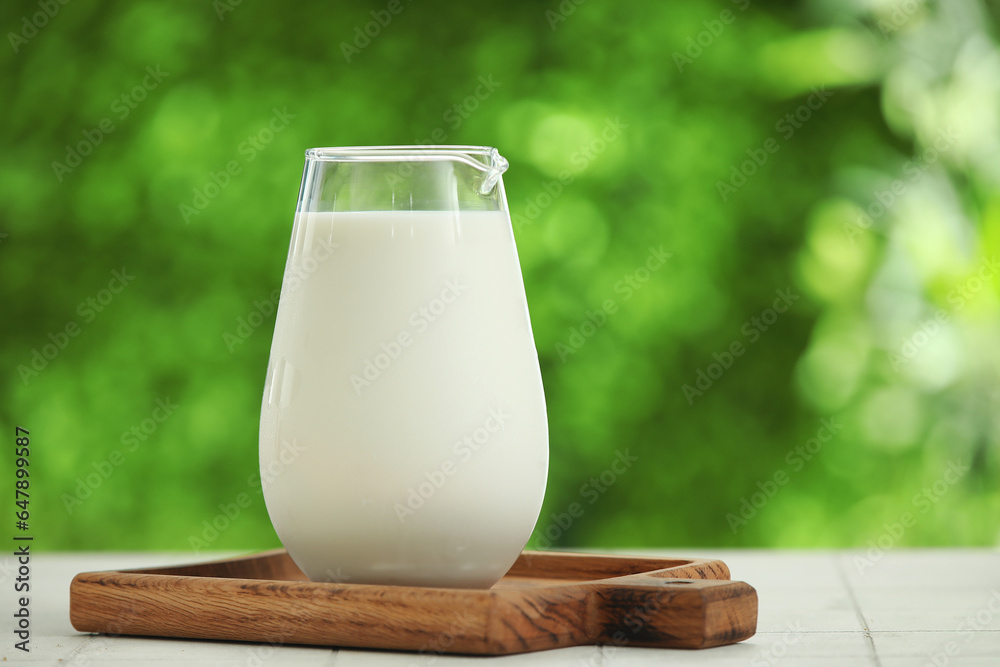 Wooden board with jug of fresh milk on white tile table outdoors