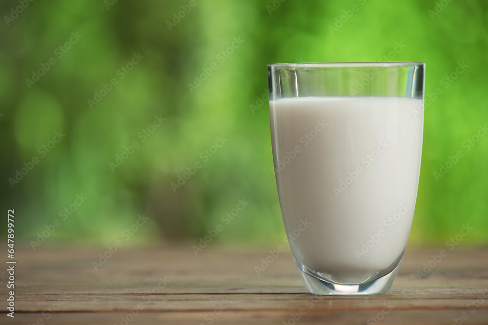 Glass of fresh milk on wooden table outdoors