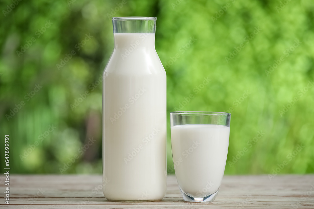 Glass and bottle of fresh milk on white wooden table outdoors