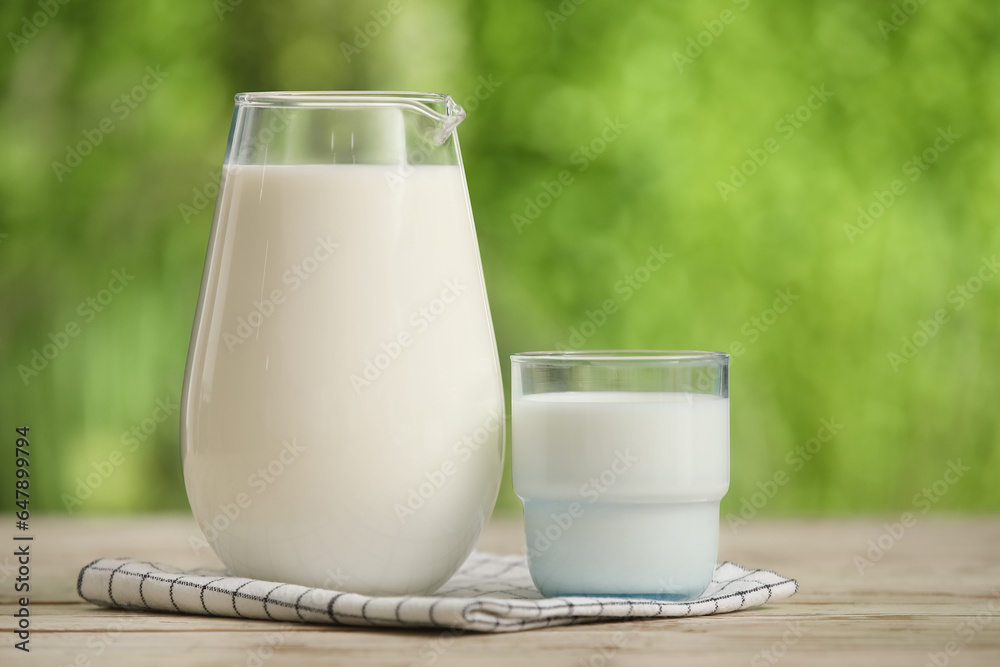 Glass and jug of fresh milk on white wooden table outdoors