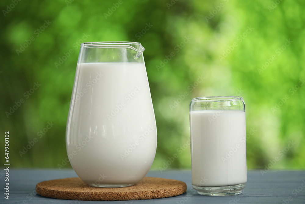 Glass and jug of fresh milk on grey wooden table outdoors