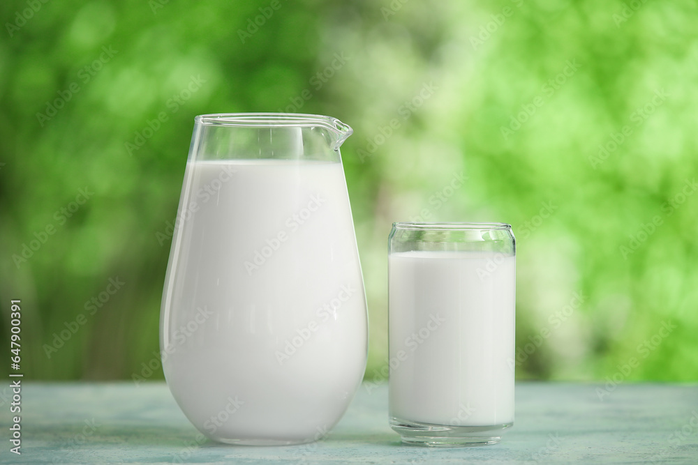 Glass and jug of fresh milk on blue table outdoors