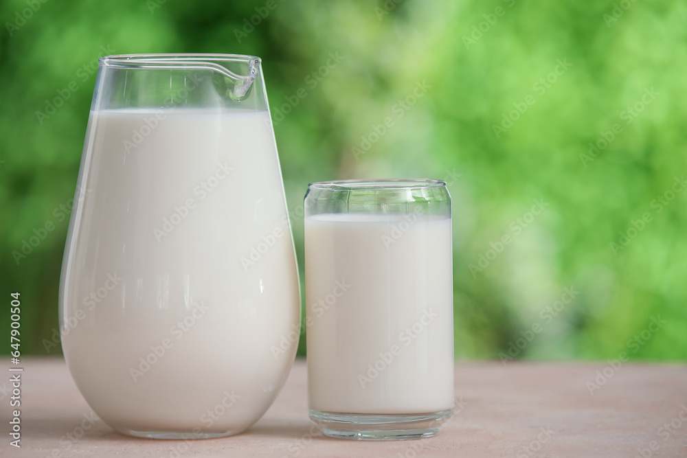 Glass and jug of fresh milk on beige table outdoors