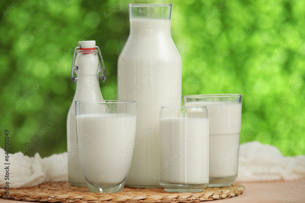 Glasses and bottles of fresh milk on beige table outdoors