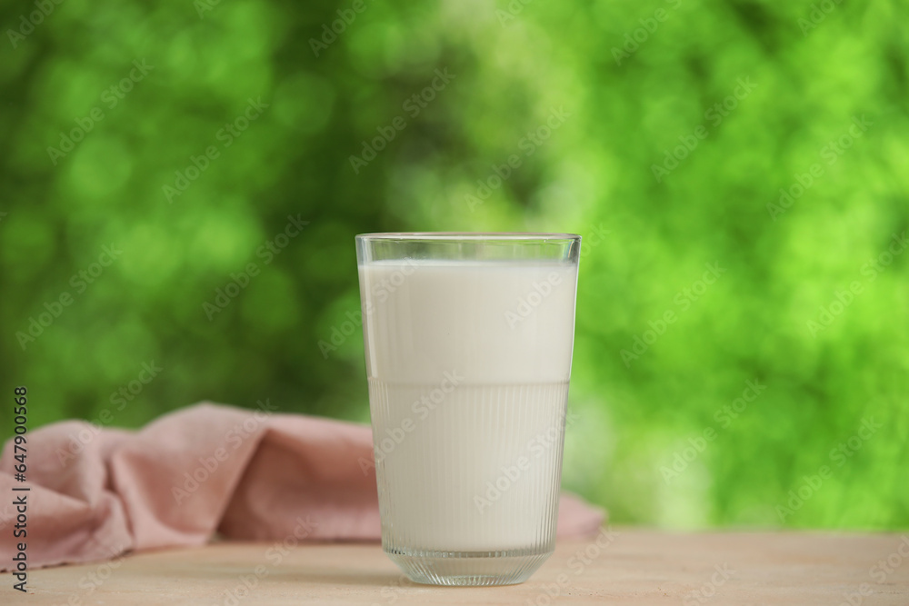 Glass of fresh milk on beige table outdoors