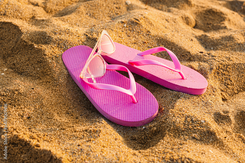 Stylish flips flops with sunglasses on sand at resort