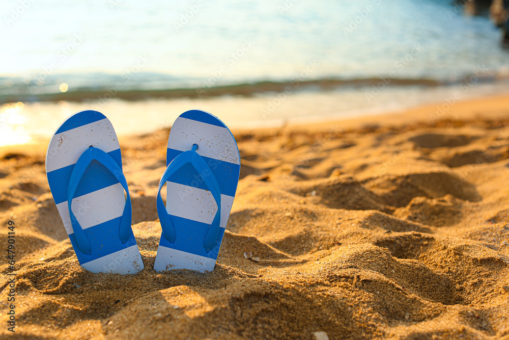 Stylish flips flops on sand near ocean at resort