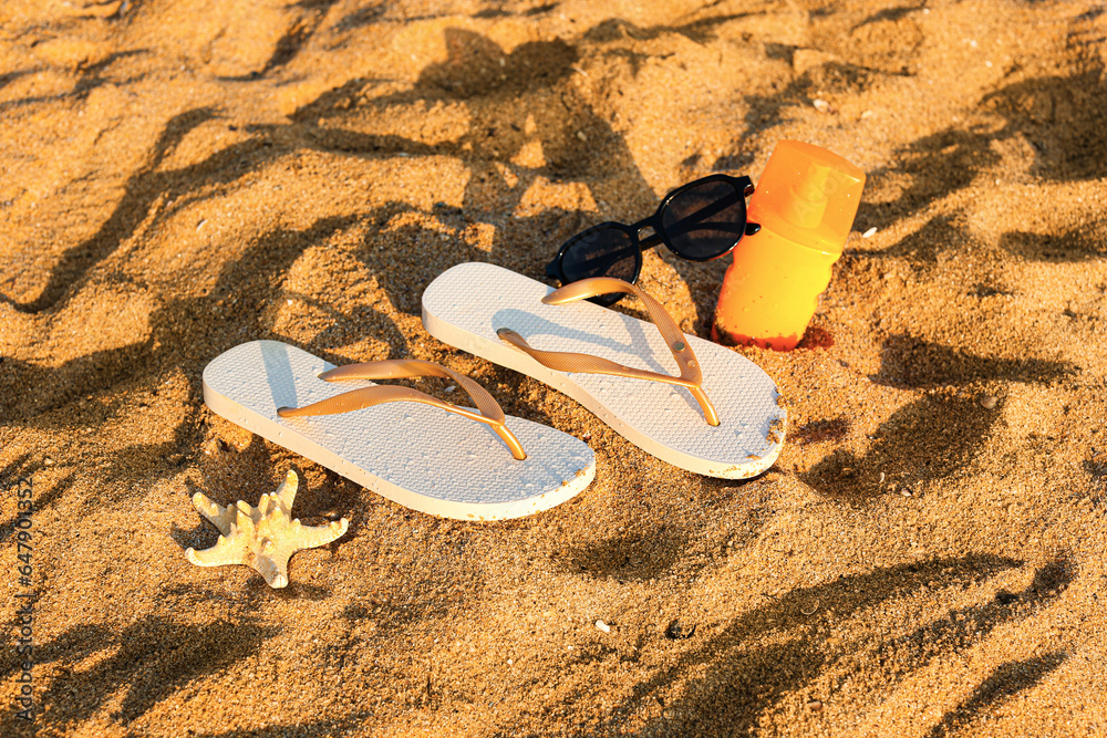 Stylish flips flops with sunglasses, sunscreen cream and starfish on sand at resort