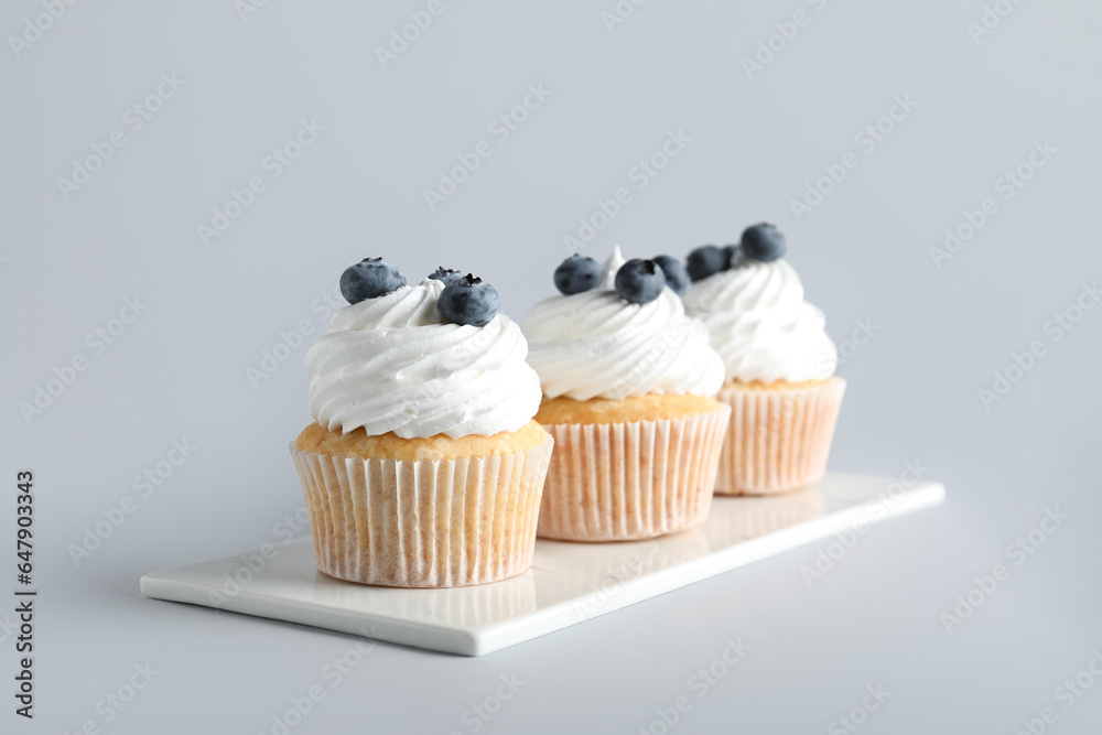 Board of tasty cupcakes with blueberries on grey background