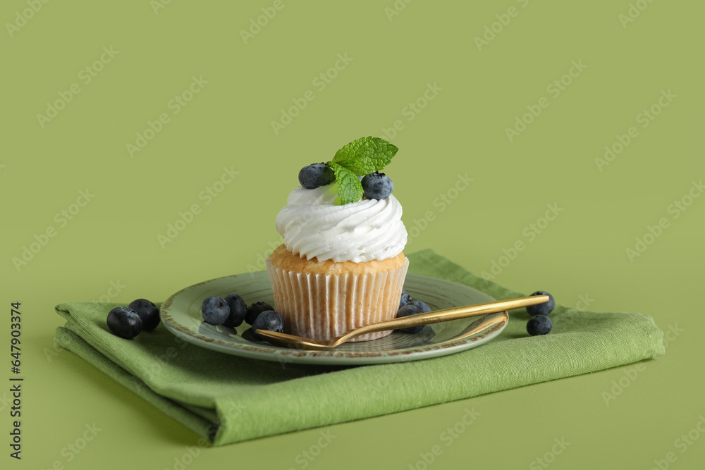 Plate of tasty cupcake with blueberries on green background