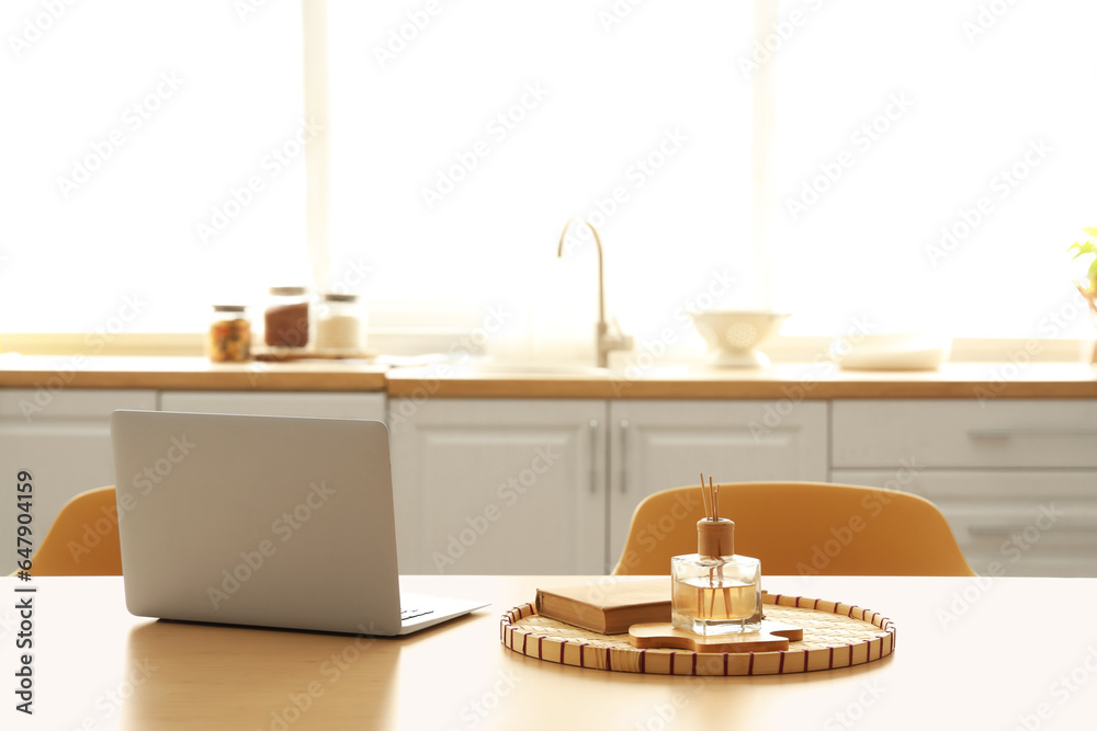 Laptop with book and reed diffuser on dining table in kitchen