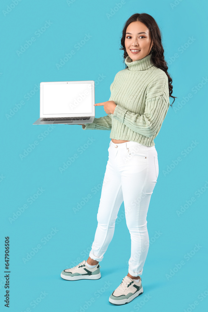 Young Asian woman with laptop on blue background