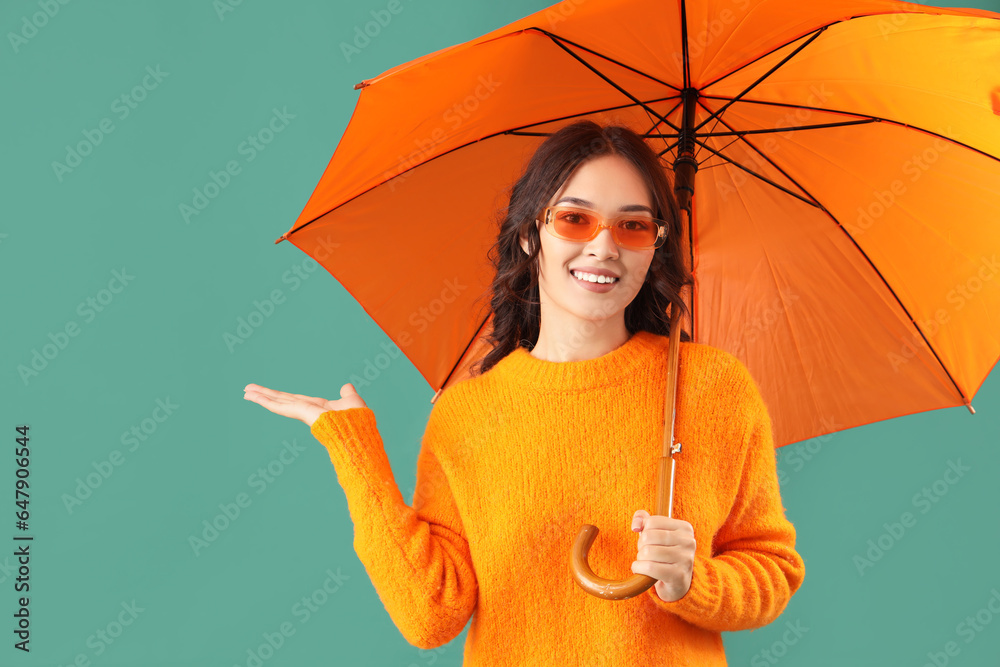 Stylish young Asian woman in fall clothes with umbrella on green background