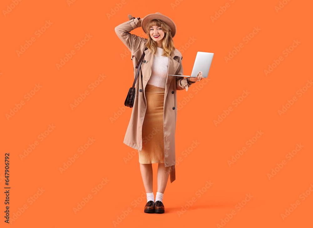 Stylish young woman in fall clothes with laptop on orange background