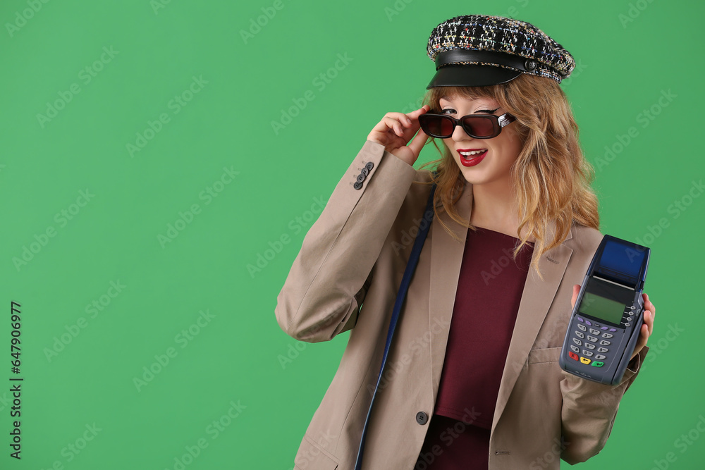 Stylish young woman in fall clothes with payment terminal on green background