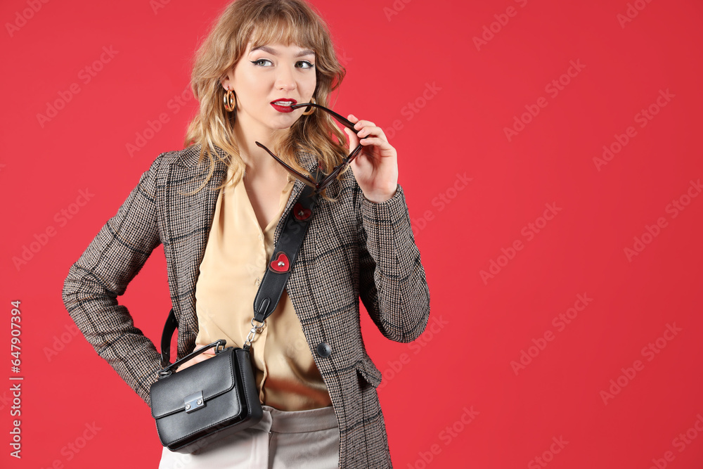 Stylish young woman in fall clothes with sunglasses on red background