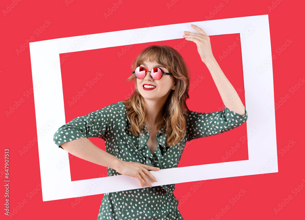 Young woman in sunglasses with frame on red background