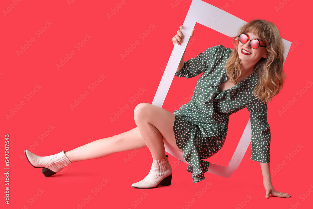 Young woman in sunglasses with frame on red background