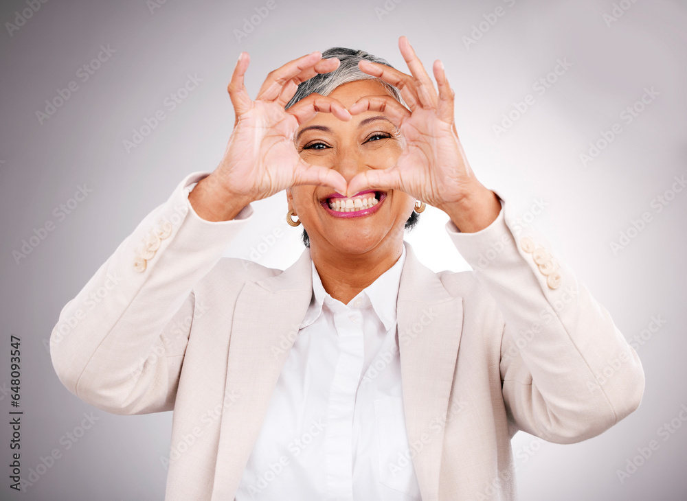 Hands in heart, business and portrait of woman for success, support and charity in studio. Success, corporate and face of mature person with hand gesture for love, yes and emoji on gray background