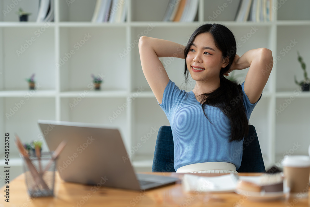 Asian woman sitting happily at work smiling relaxing and chatting with friends on social media search for information on laptop take notes in a notebook while sitting on a desk in his office at home