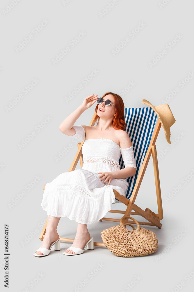 Young woman with sunglasses relaxing in deck chair on light background