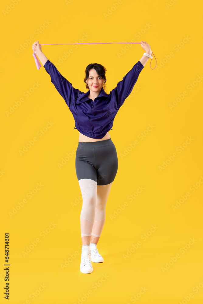 Sporty young woman with jumping rope on yellow background