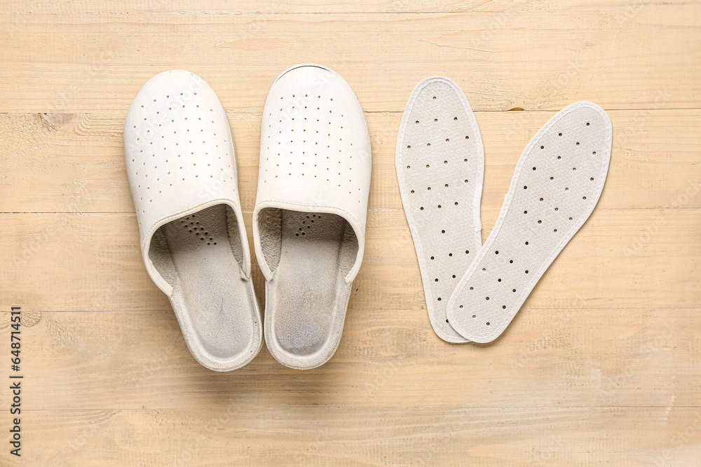 Pair of slippers and orthopedic insoles on wooden background