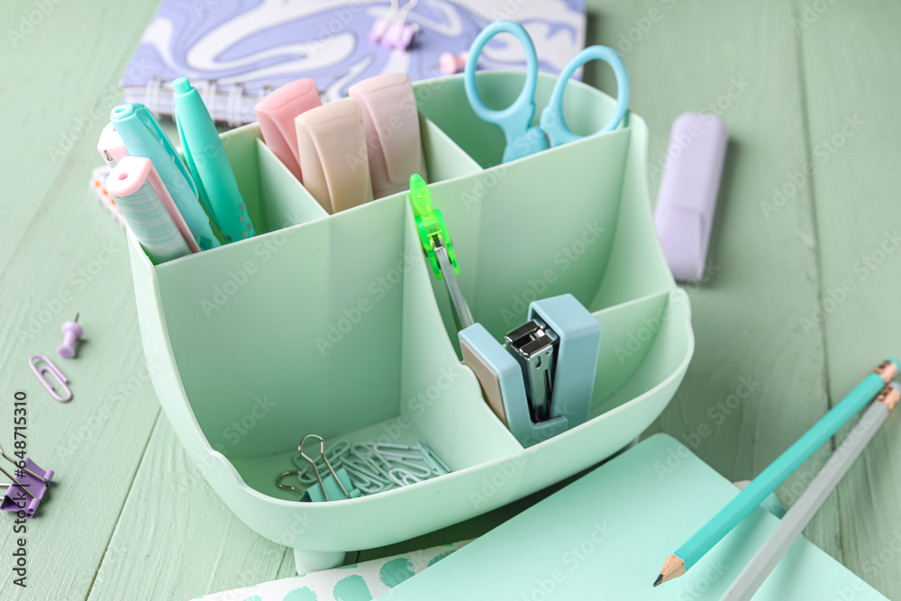 Holder with different stationery on color wooden background, closeup