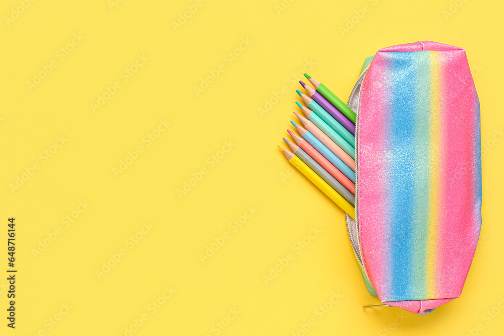 Colorful case with pencils on yellow background