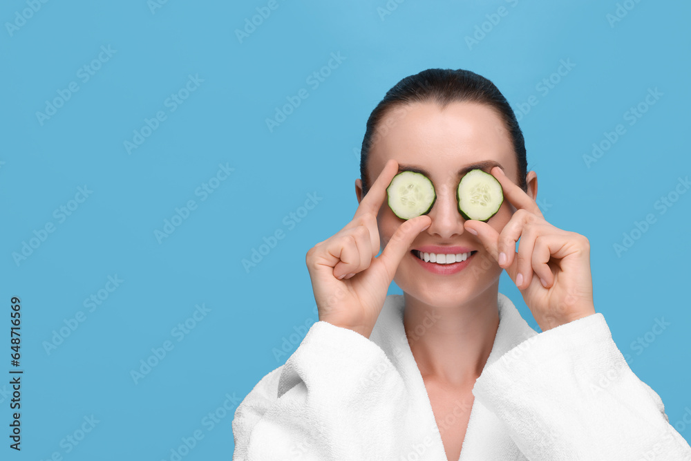 Beautiful woman covering eyes with pieces of cucumber on light blue background, space for text