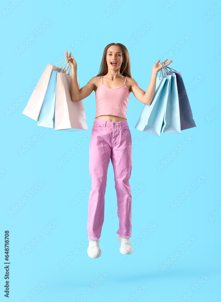 Young woman with shopping bags jumping on blue background