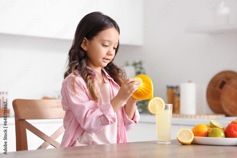 Little Asian girl making fresh citrus juice at table in kitchen