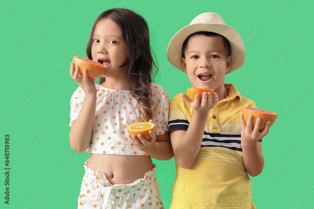 Little Asian children eating fresh oranges and grapefruits on green background