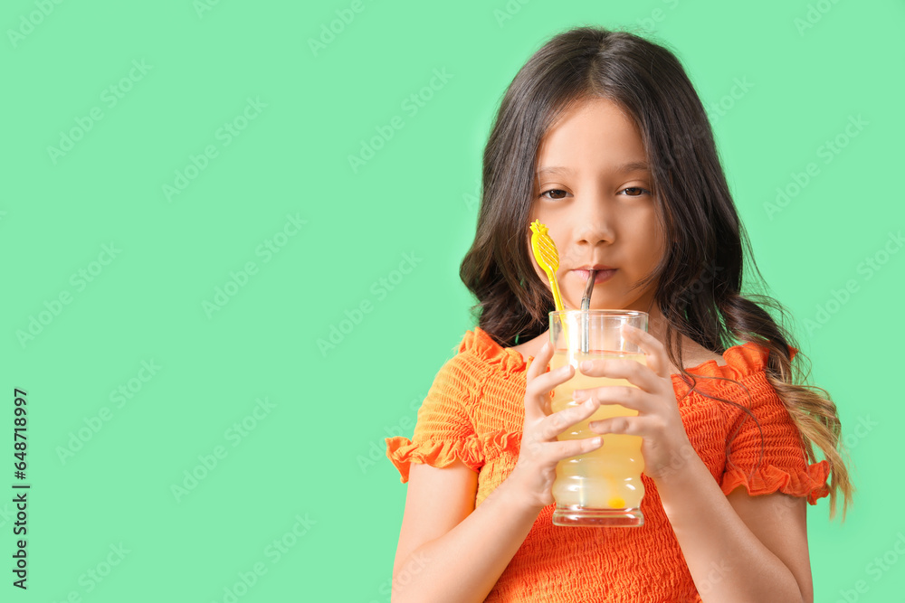 Little Asian girl with glass of fresh citrus juice on green background