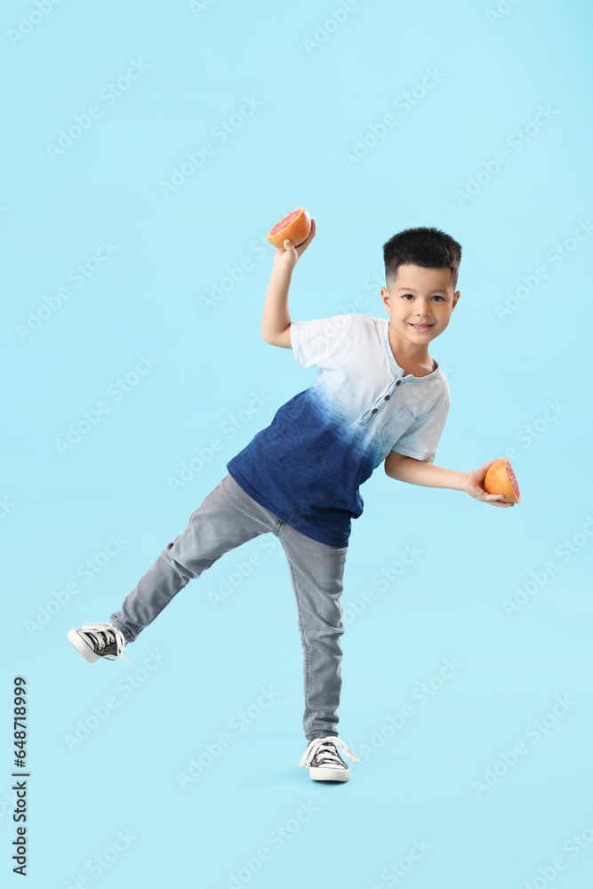 Little Asian boy with slices of fresh grapefruit on blue background