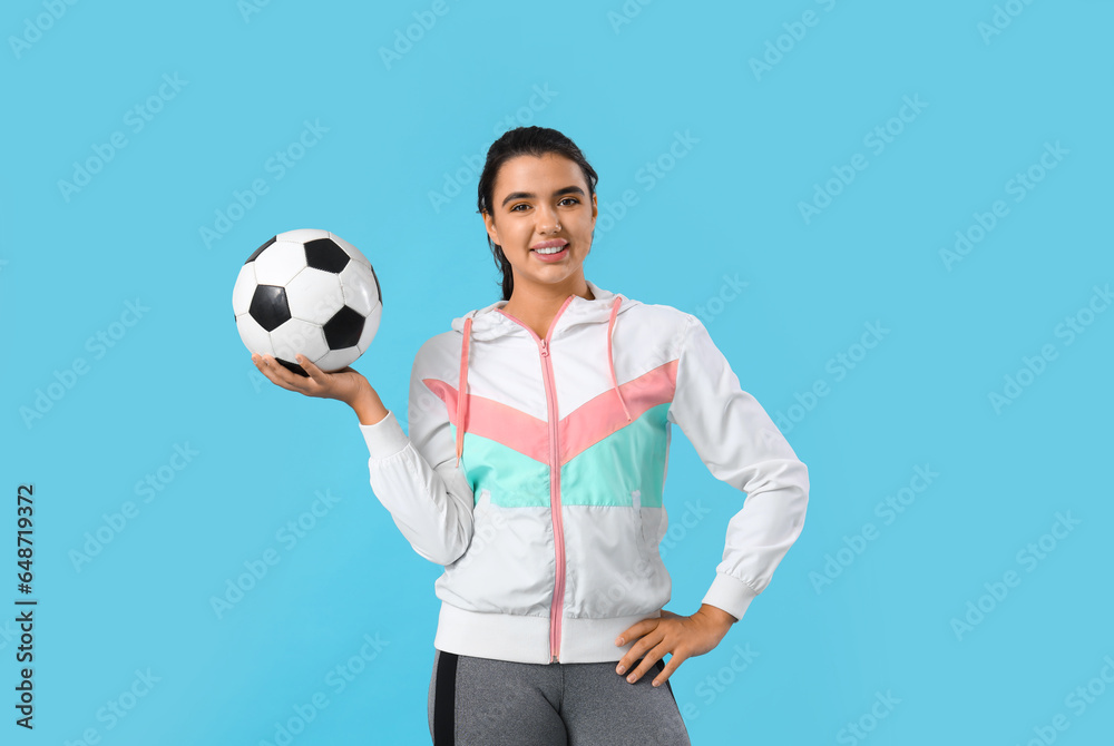 Sporty young woman with soccer ball on blue background