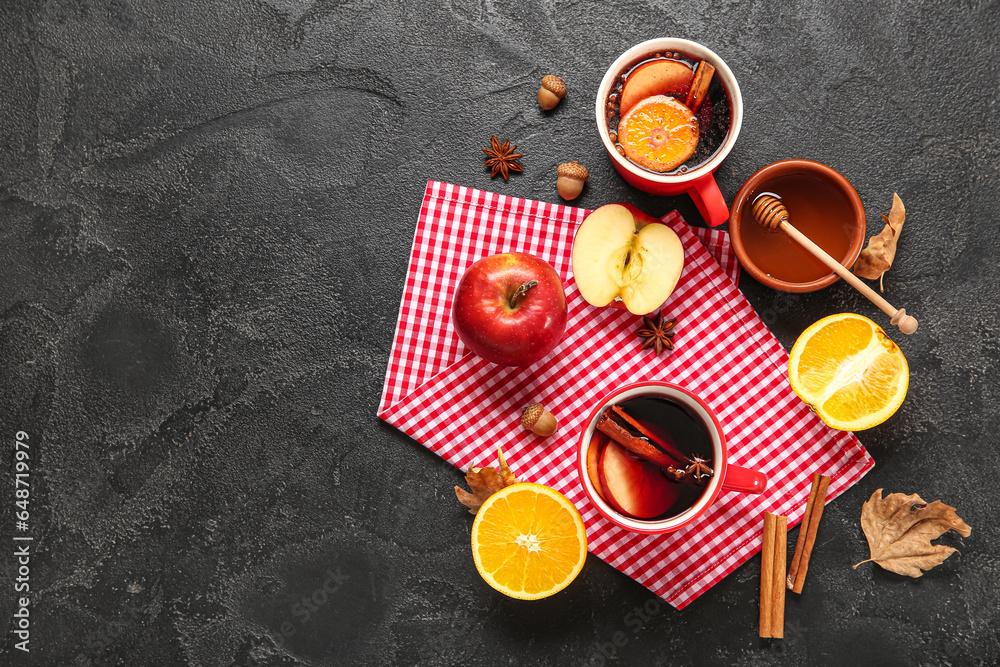 Cups of hot mulled wine with apple and orange on black background