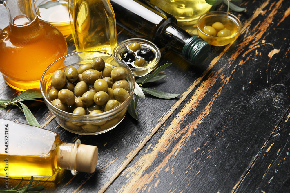 Different glassware with olives and oil on black wooden background